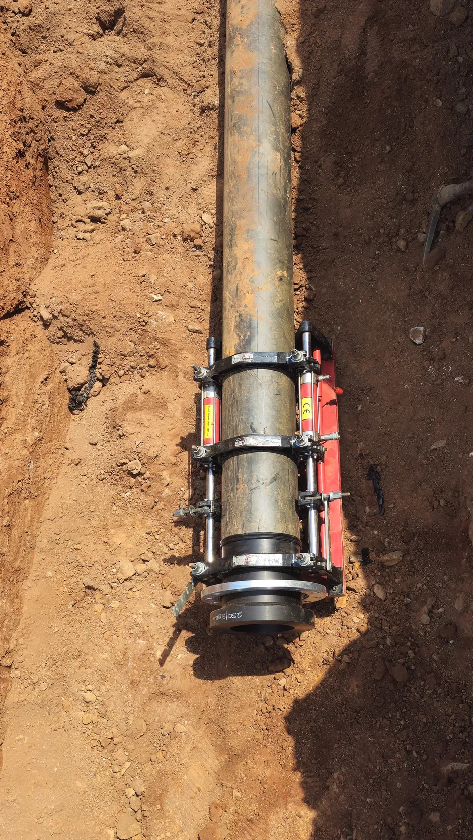 Red butt-fusion clamp fusing HDPE pipe in trench